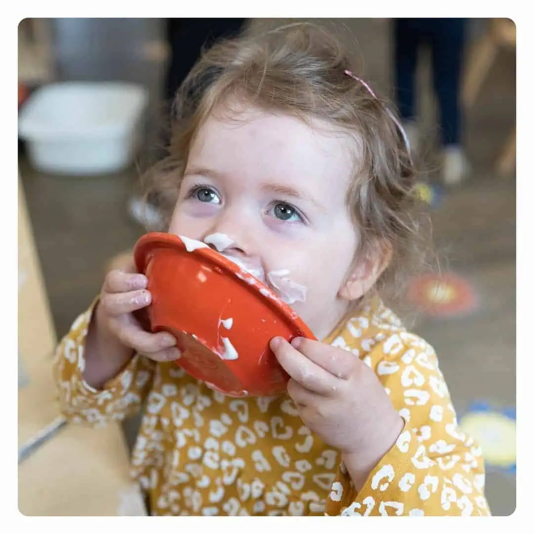 Cute young girl with curly hair enjoying her meal at Monkey Puzzle Day Nursery & Preschool Lightwater, showcasing a fun and nurturing early childhood environment.